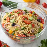 Colorful spaghetti salad recipe in glass bowl with fresh vegetables and Italian dressing