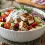 Chicken salad with tzatziki sauce in white bowl with fresh vegetables