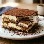 Classic tiramisu slice 45 degree showing mascarpone layers espresso savoiardi and cocoa on white plate