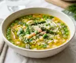 Plated spring minestrone with peas and herbs at 45-degree angle with Parmesan and olive oil